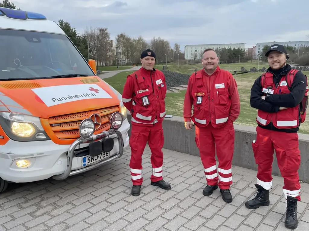 Kolme SPR Itä-Helsingin ensiapupäivystäjää punaisissa asuissa osaston auton vieressä